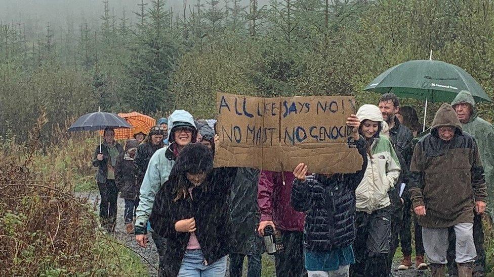 protestors on a forest road holding no mast placard