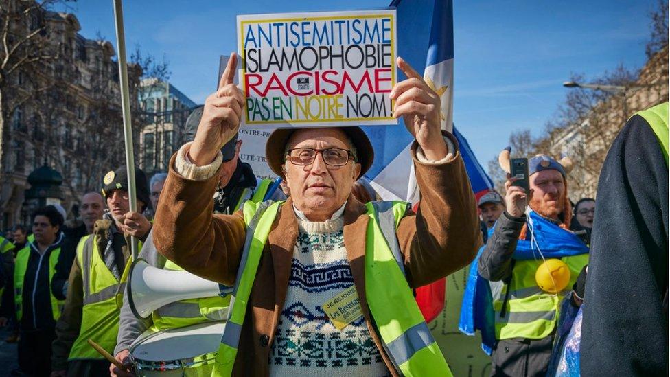 A protester holds up a sign that says 'Anti-Semitism, Islamaphobia, racism is not us'