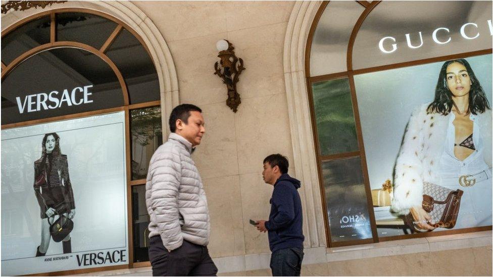 Pedestrians walk past advertisements for Versace, left, and Gucci at the Trang Tien Plaza luxury shopping center in downtown Hanoi, Vietnam, on Tuesday, Feb. 27, 2024.