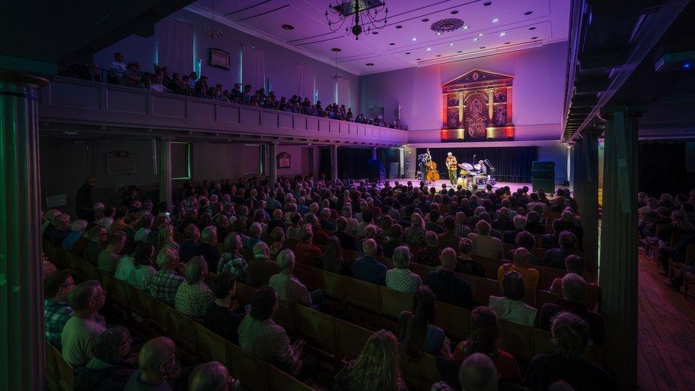 A wide shot of St George's in Bristol with audience members seated and the Bill Frisell trio playing on stage