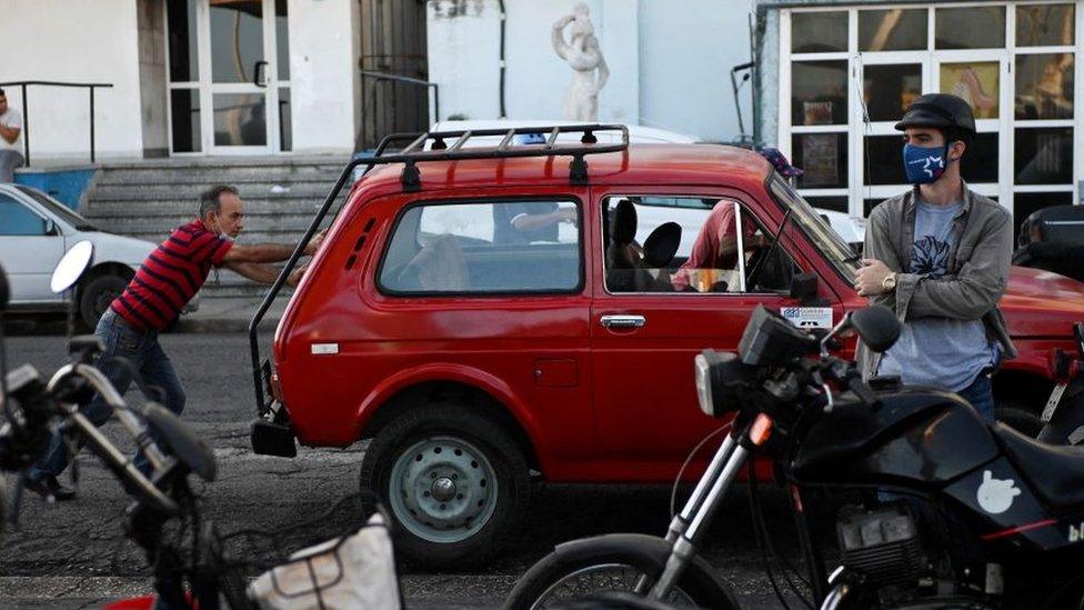 A man stands in front of a red car being pushed by two other men in Havana on 22 March 2022