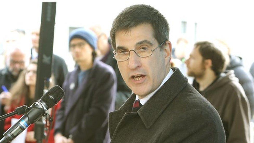 Anthony Forster with short dark hair wearing a black coat in a crowd of people