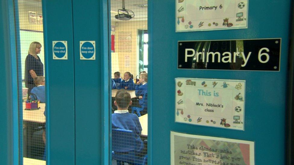 A teachers stands in a classroom with schoolchildren