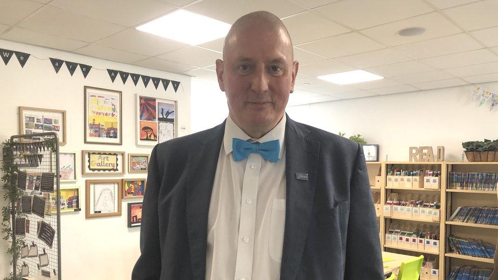 David Baker in a suit with bowtie standing in a classroom