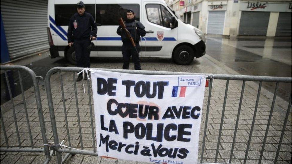 Police officers stand guard behind a barricade with a sign reading "Wholeheartedly with the police - Thank you" in Seine-Saint-Denis (November 19, 2015)