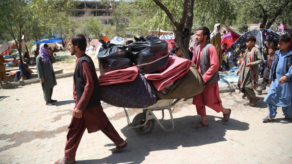 Afghan displaced people who fled from their homes during the fighting carry their belongings in a public park in Kabul