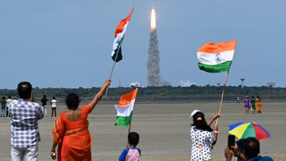 Children waving Indian flags as rocket launches in background