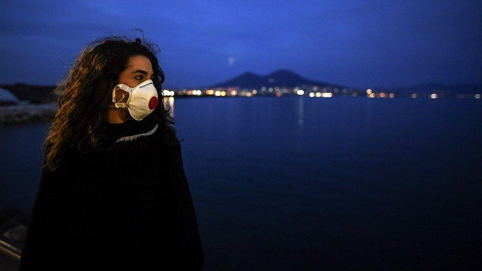 A woman wearing antivirus masks, to protect herself from the Coronavirus (Covid 19) waiting for a super moon walks at sunset on the Naples waterfront in front of the Vesuvius volcano.