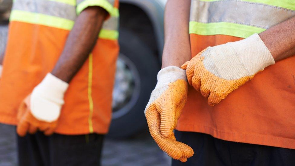 An image of two refuse workers, dressed in orange clothing