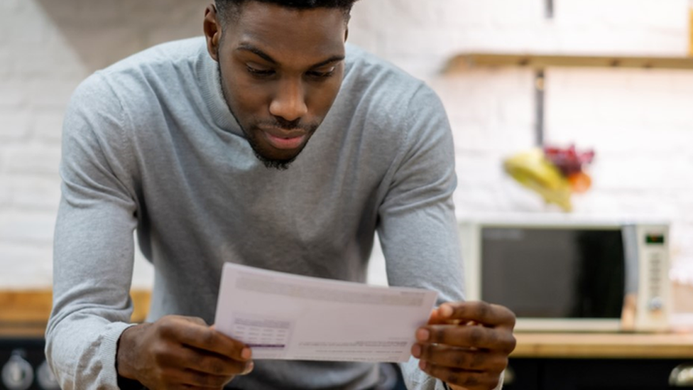 Man in kitchen looking at paper bill