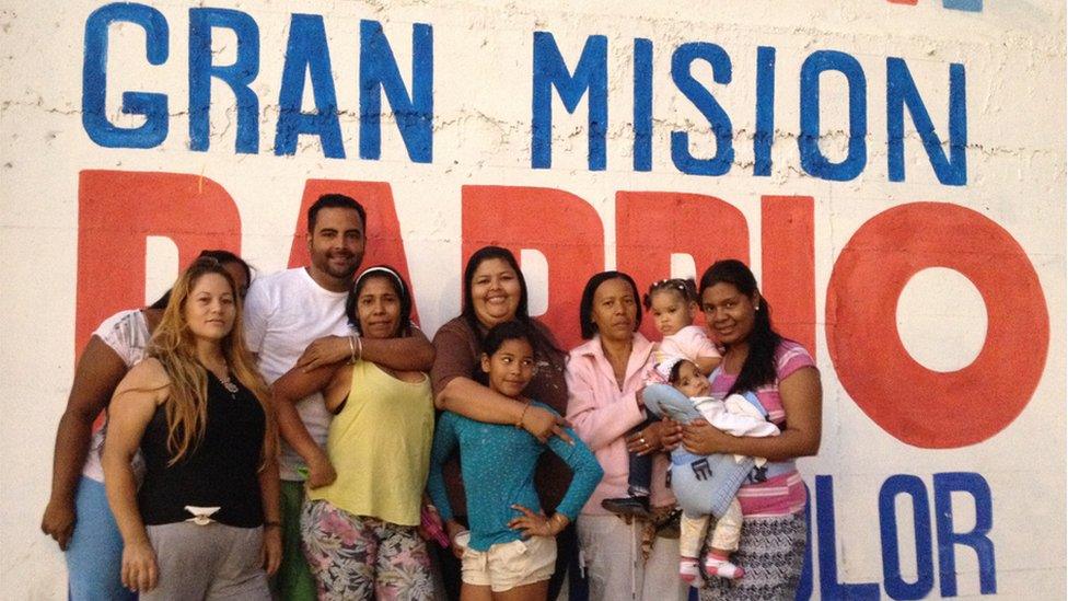 A group of residents pose before a sign reading "Gran Mision Barrio" ("Great Neighbourhood Mission)