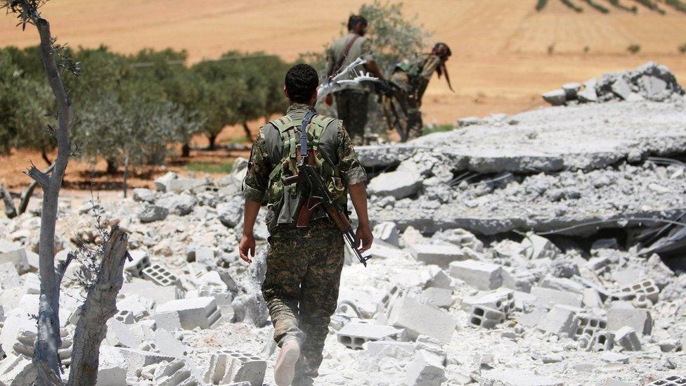 Syrian Democratic Forces (SDF) fighters walk through remains of Islamic State position outside Manbij (11 June 2016)