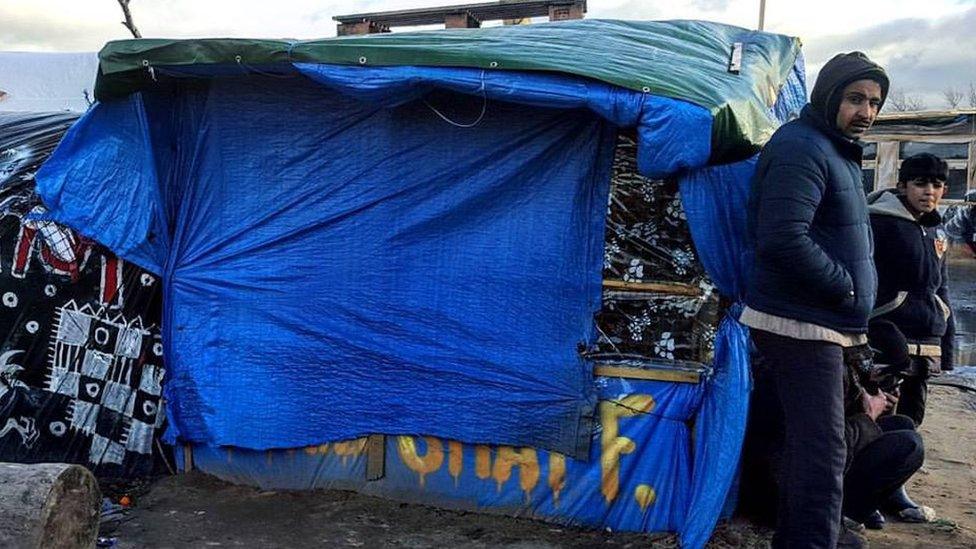 Migrants stand outside a shelter in the Calais camp