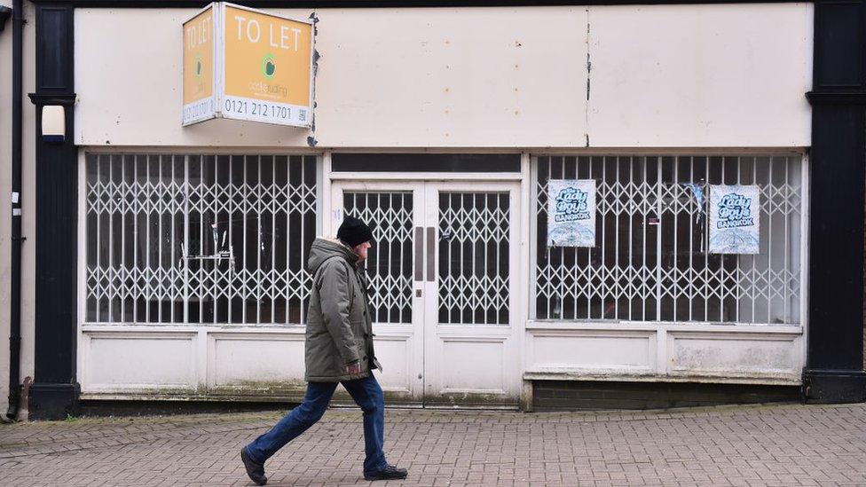 Man walking past a boarded up shop