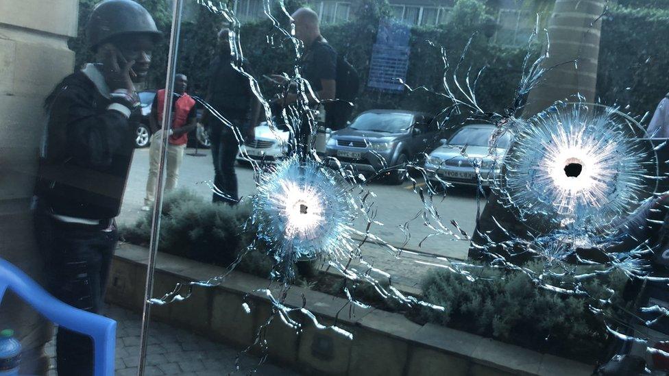 A soldier takes cover next to bullet holes during an ongoing gunfire and explosions in Nairobi, Kenya