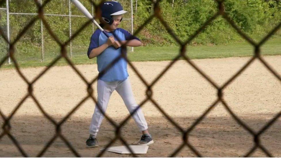 Girl playing baseball, with fencing