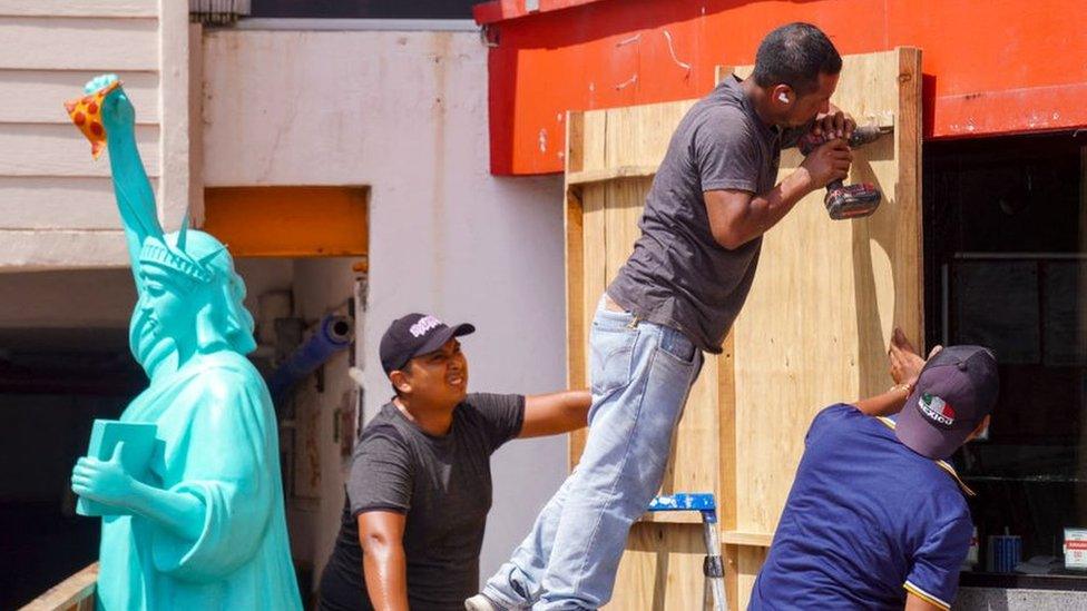 Workers nail wooden boards to the outside of a building in Mexico, ahead of the arrival of Hurricane Milton on 7 October 2024