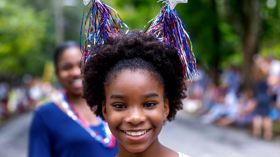 A girl in a parade smiles wile wearing stars and stripes headband