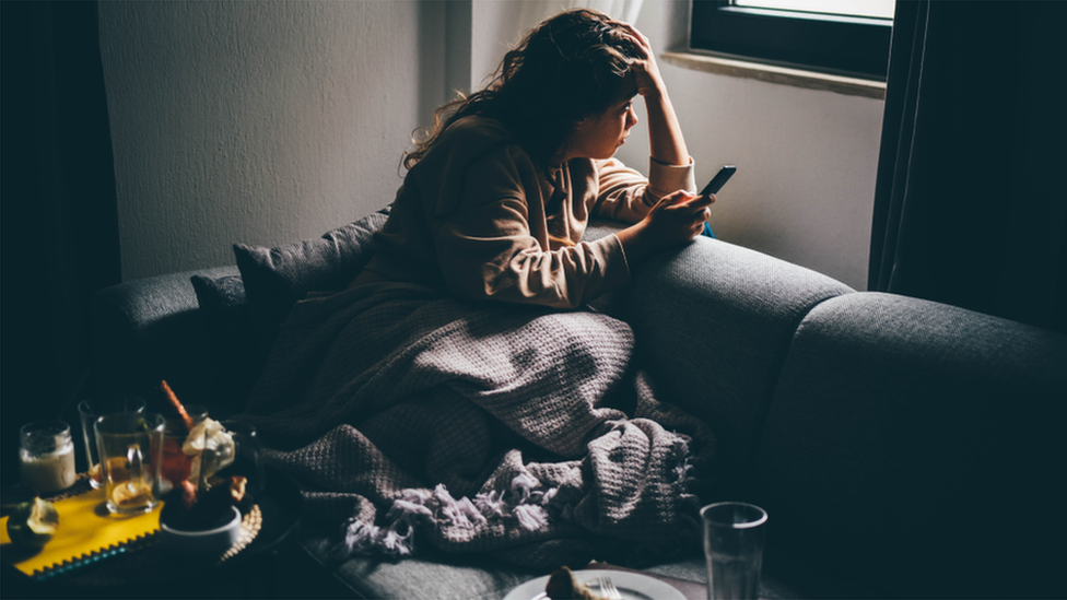 Woman sits on a sofa with head in hand