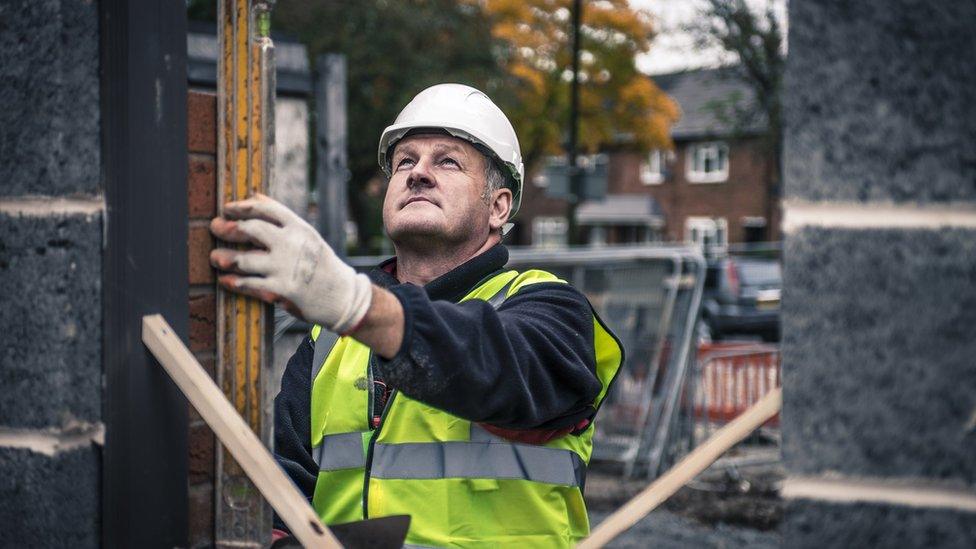 A builder in a high-vis jacket levelling bricks