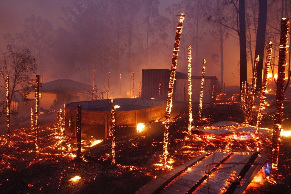 Remains of a structure burned by a bushfire continue to smoulder