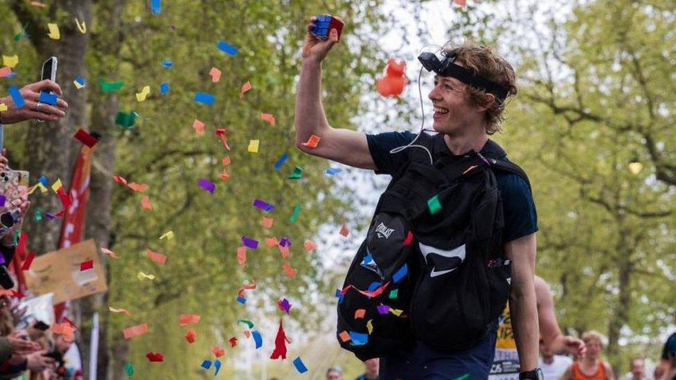 George Scholey running along the course carrying a Rubik's Cube, which he is showing to the crowd