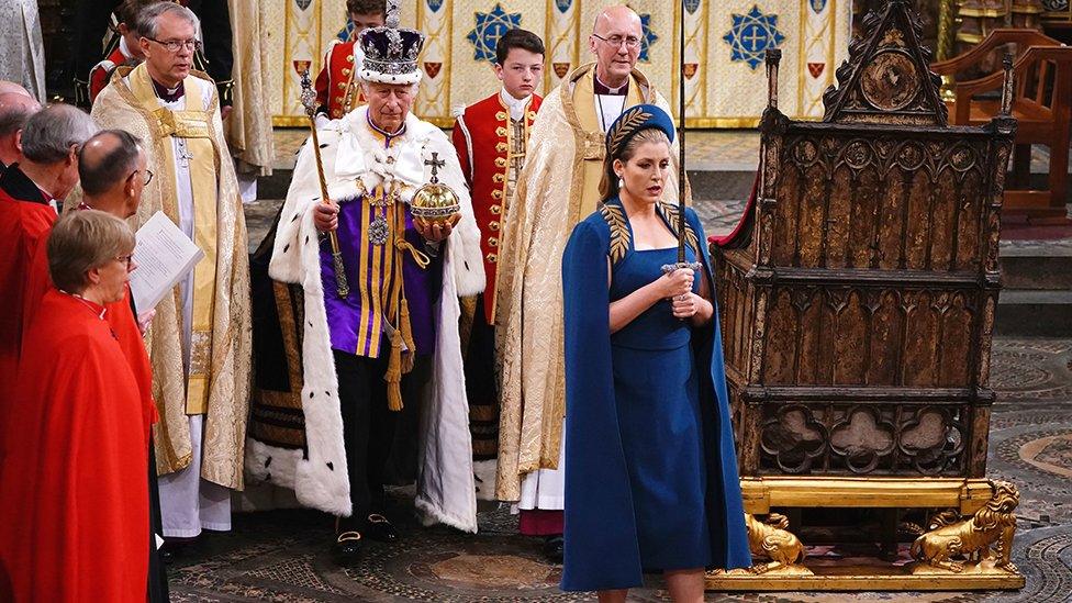 Lord President of the Council, Penny Mordaunt, holding the Sword of Offering walking ahead of King Charles III