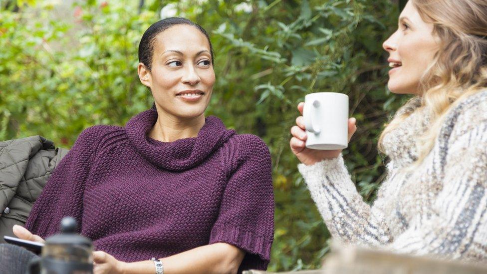 two women chatting, one holding phone