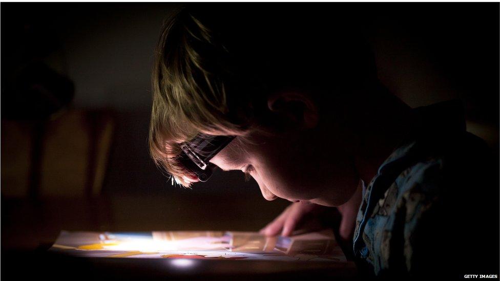 A photo of a boy reading with a torch