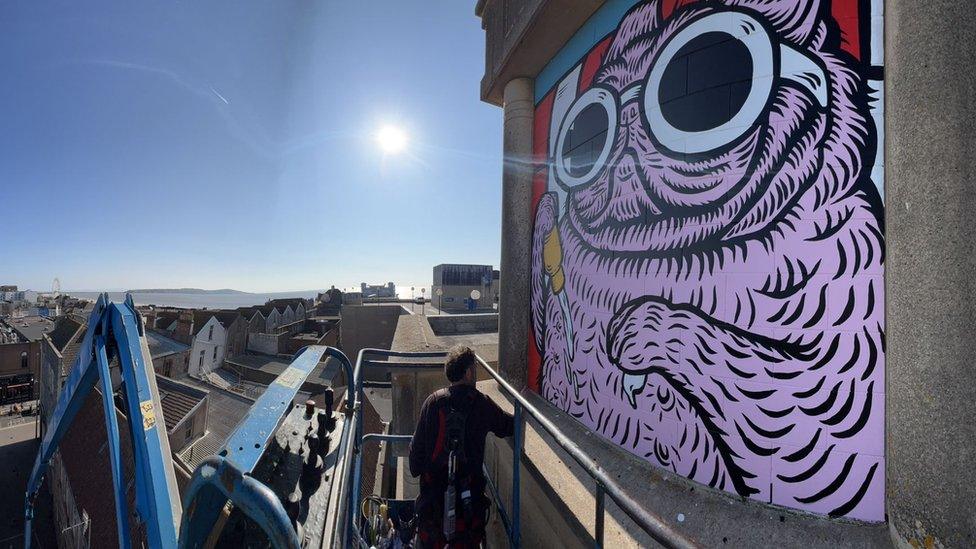 A pink dog mural being painted on a building