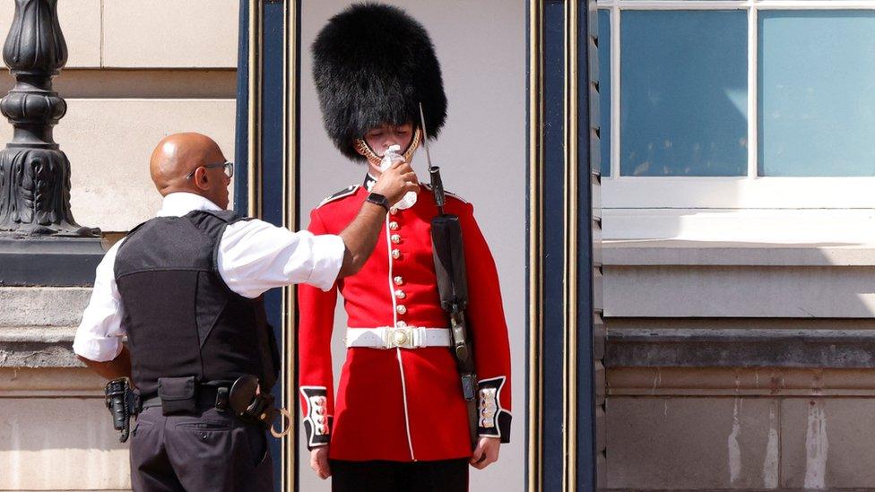 A member of the Queen's Guard wearing a bearskin hat receives water to drink during the hot weather, outside Buckingham Palace in London