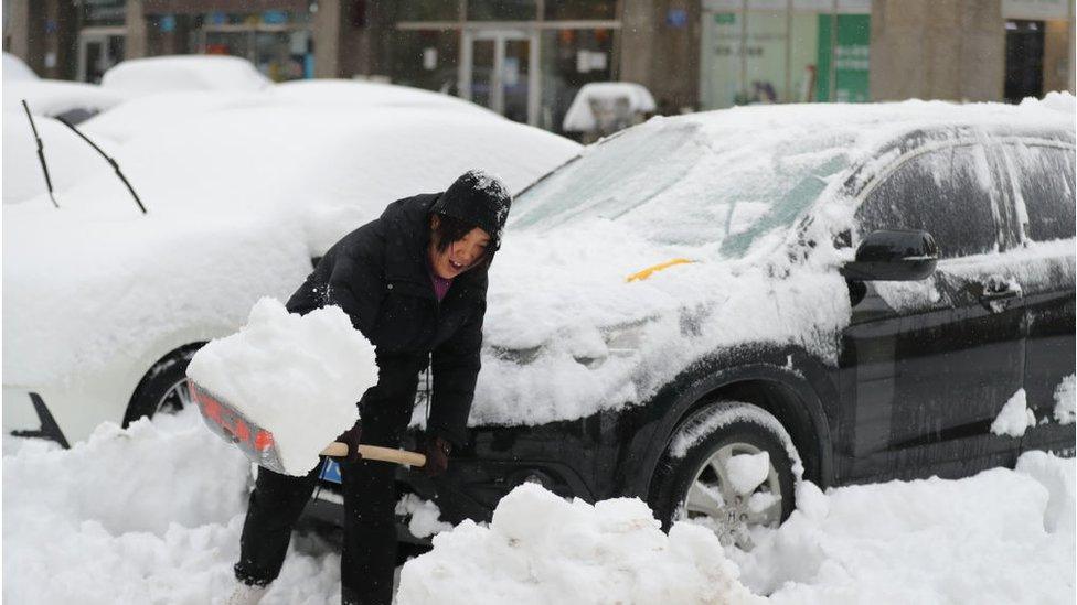a woman shovels snow outside on the street