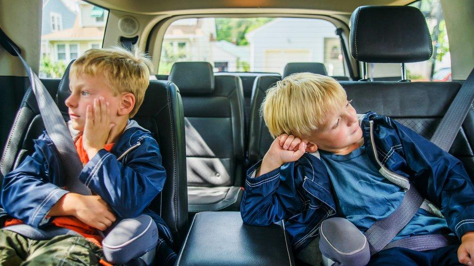 Two boys bored in the back of a car