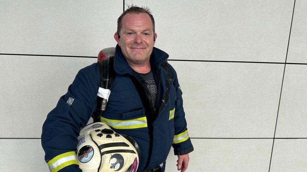 Ronnie Sherratt (short brown hair) with firefighters' protective clothing and helmet