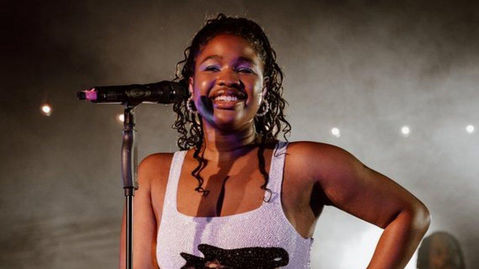 Debbie performs onstage, she's wearing a sequin lilac mini dress with a killer whale print. She's smiling, her hair is pulled back off her face, soft curls rest on her shoulders.