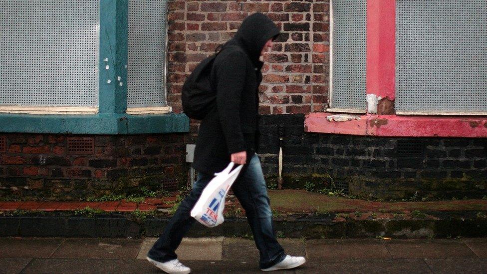 Man walking past some boarded up houses