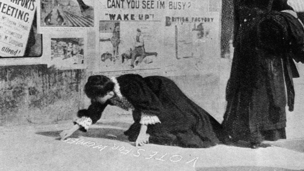 Annie Kenney painting a pavement with a slogan, 'Votes For Women' in 1907