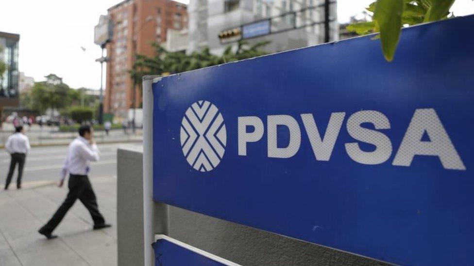 People walk past a sign with a PDVSA logo at its gas station in Caracas on 28 October, 2015.