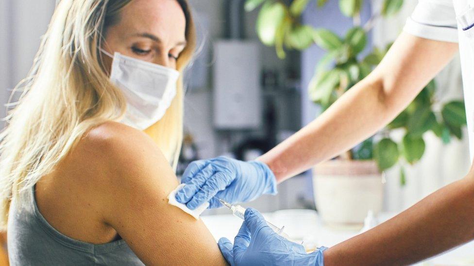 Close-up at home, the doctor holds a syringe and uses cotton wool to inject a patient in a medical mask