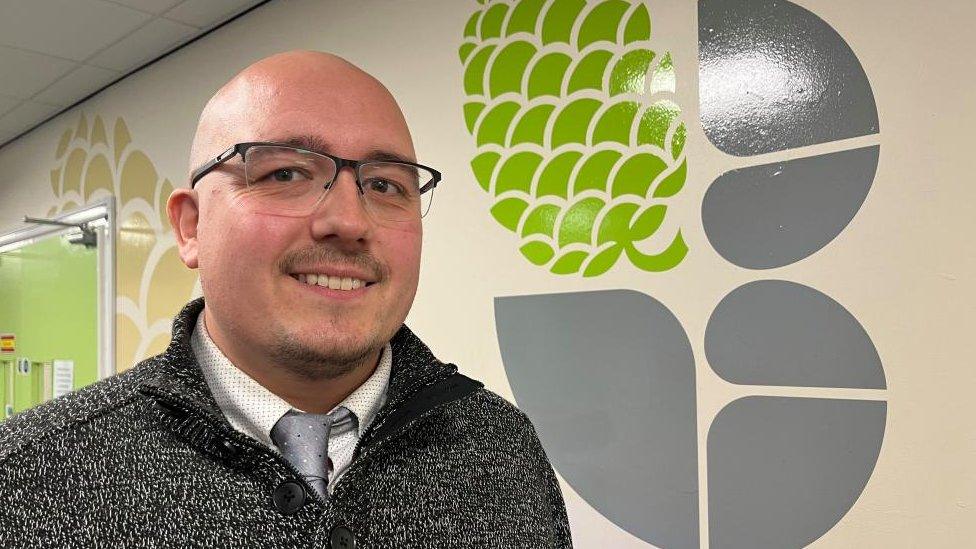 Head of Personal, Social, Health Education Chris Brooks standing by school logo.