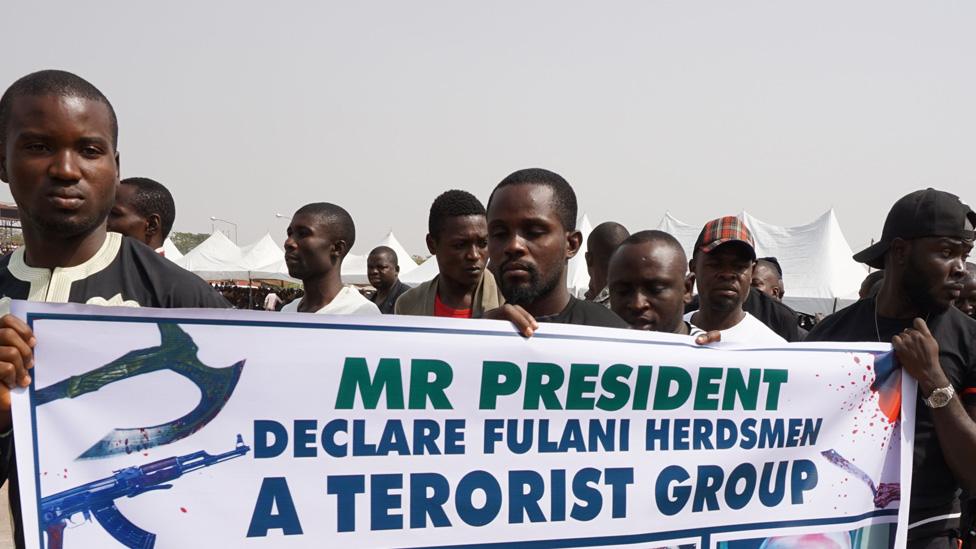 Mourners carry banner who shows picture of people who died following clashes between Fulani herdsmen and natives of Guma and Logo districts at Ibrahim Babanginda Square in the Benue State capital Makurdi, on January 11, 2018, during a funeral service