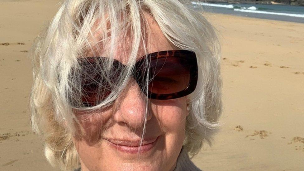 A woman wearing sunglasses, smiling on the beach