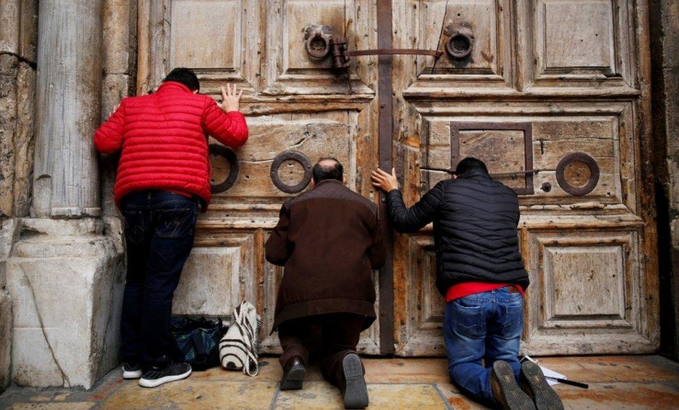 Men kneel and pray in front of the church's doors in Jerusalem's Old City