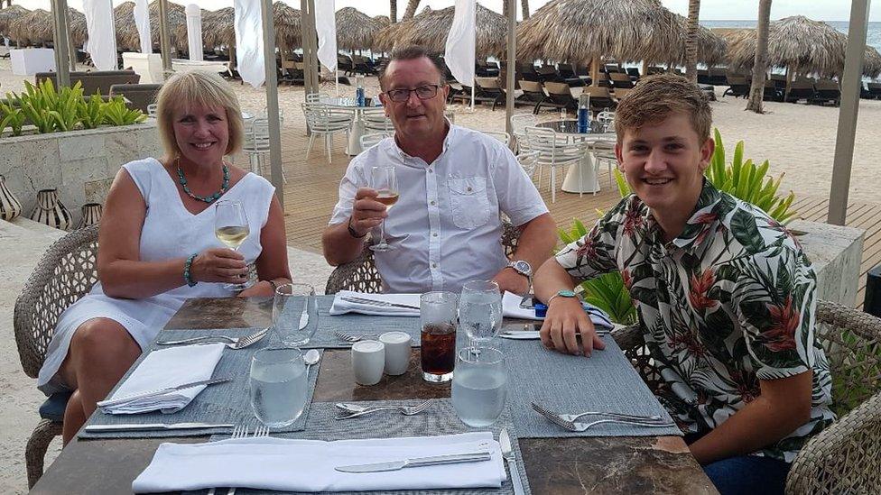 A woman with blonde hair, a man with brown hair and a boy in a Hawaiian skirt