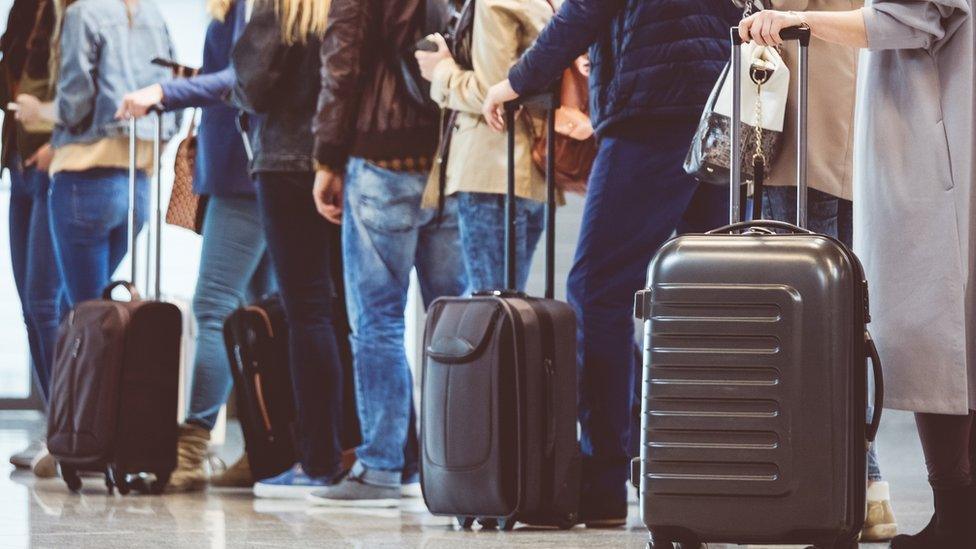 Passengers queuing with their luggage in an airport.