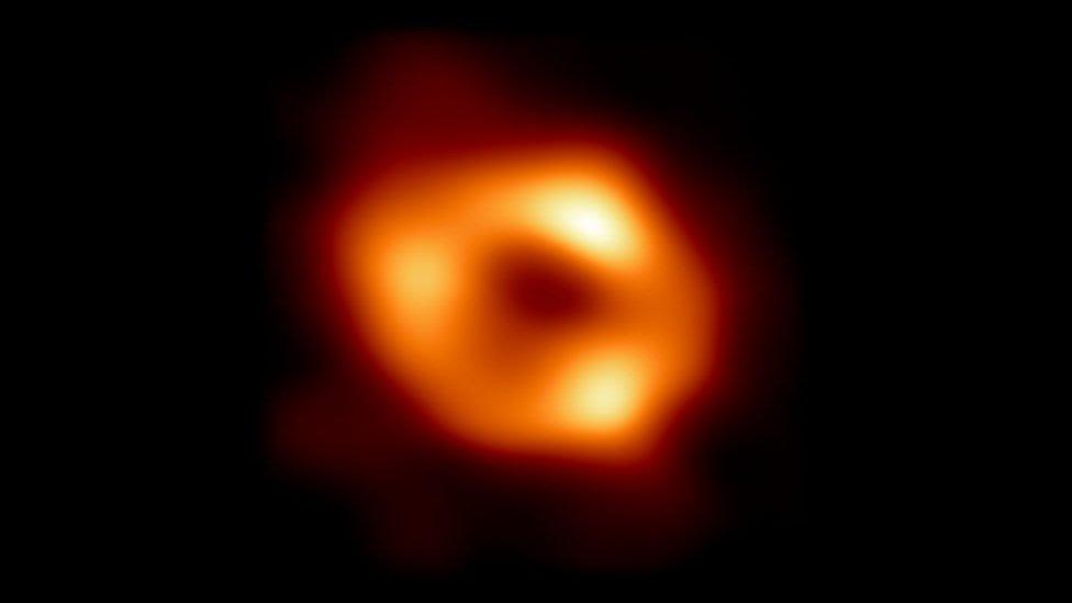 Image of black hole shown by orange light with black circle in middle