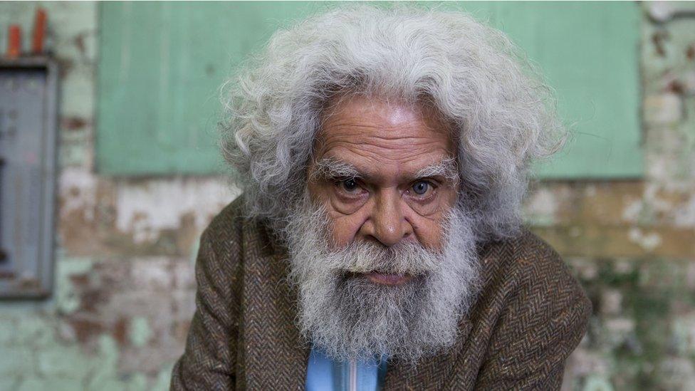 Jack Charles, with long white hair, looks straight into the camera