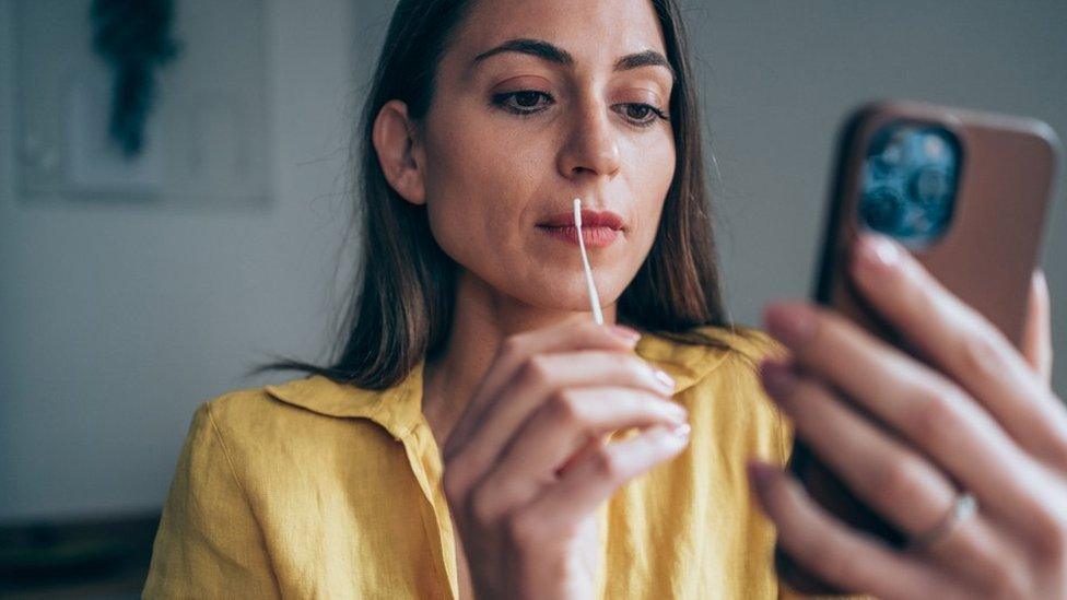 A woman swabs her throat while looking at her phone screen