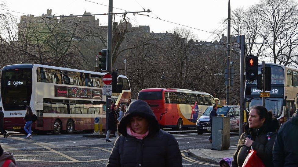 Pedestrians cross in front of buses on Princes Street