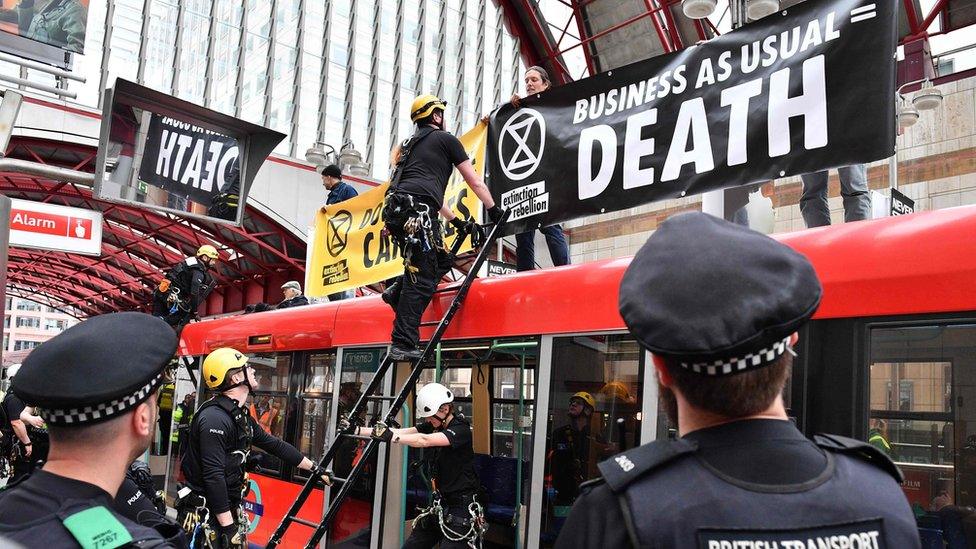 Police prepare to remove climate change activists on the roof of a DLR train at Canary Wharf station